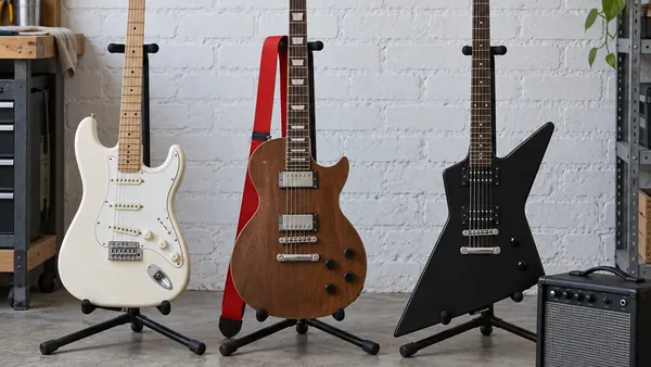 Guitarra eléctrica de iniciación apoyada en un soporte junto a un ampli pequeño